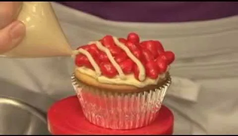 Decorating a cupcake with red frosting and white icing drizzle.