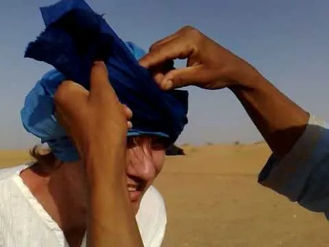 Person being assisted in wearing a blue headscarf in a desert setting.