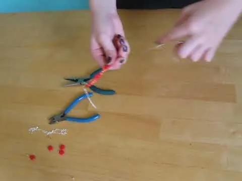 Hand crafting jewelry with pliers and beads on a wooden surface.