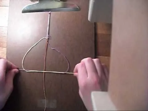 A person's hands working with strings on a wooden surface.