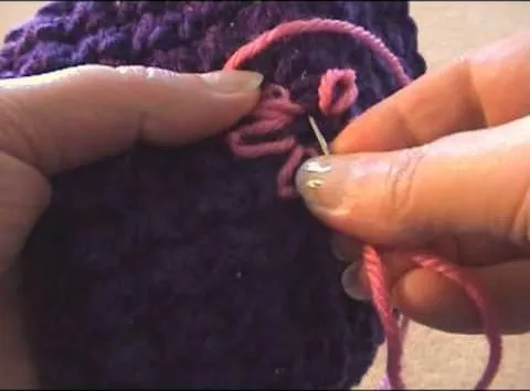 Crocheting a pink yarn loop with a needle.