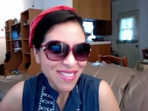 Woman wearing sunglasses and a red headband, smiling in a home setting.