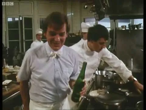 Chef holding a bottle while working in a professional kitchen.