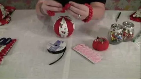 Craftsperson creating a decorative ball using red fabric and embellishments.