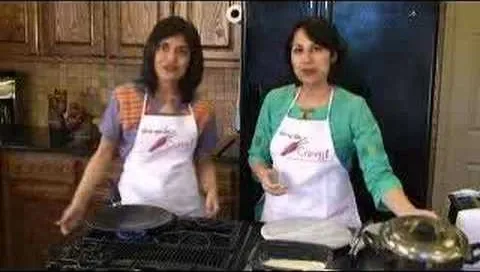 Two women cooking in a kitchen, wearing aprons.