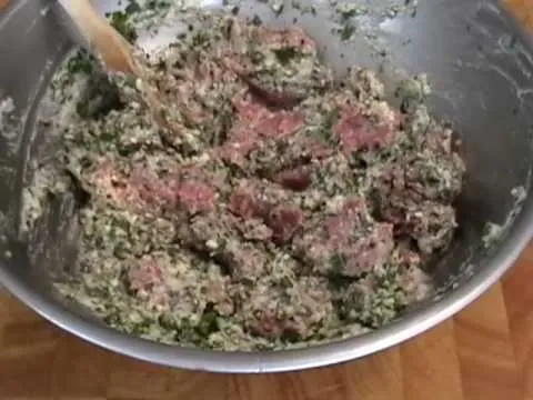 Ground meat mixture with herbs and spices in a stainless steel bowl.