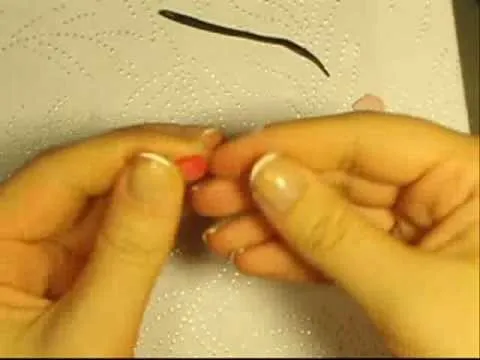 Hands manipulating small modeling material on a textured surface.