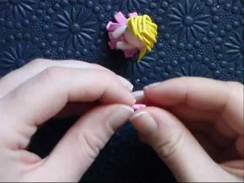 Hands crafting a small pink figurine with a blonde hairpiece.