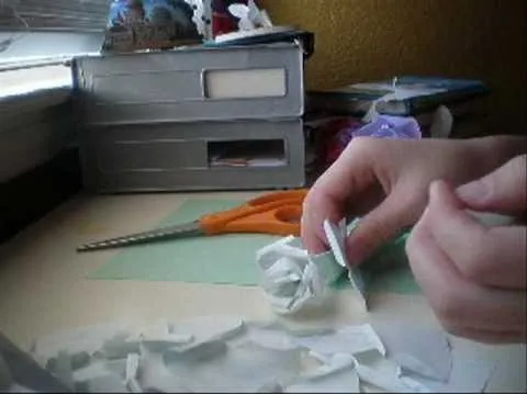 Hand crafting a paper flower on a desk with scissors and crafting materials.