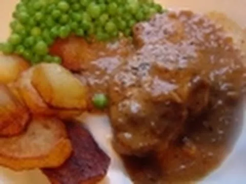 Plate of meat with gravy, green peas, and roasted potatoes.