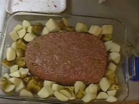 Meatloaf surrounded by diced potatoes in a baking dish.