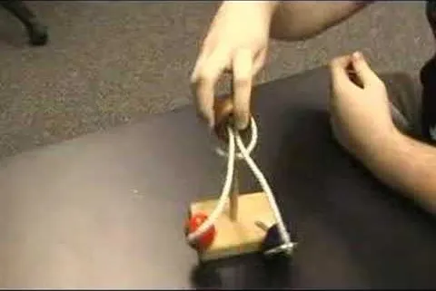 Hands demonstrating a mechanical device with pulleys and a wooden base.