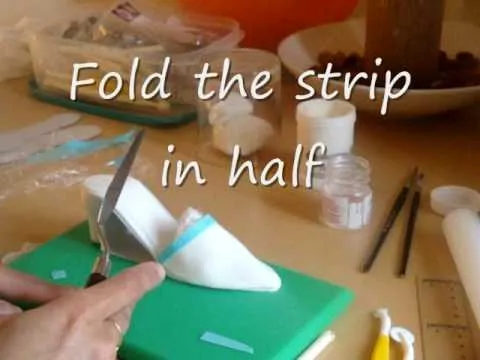 Person folding a strip of material in half on a cutting board.