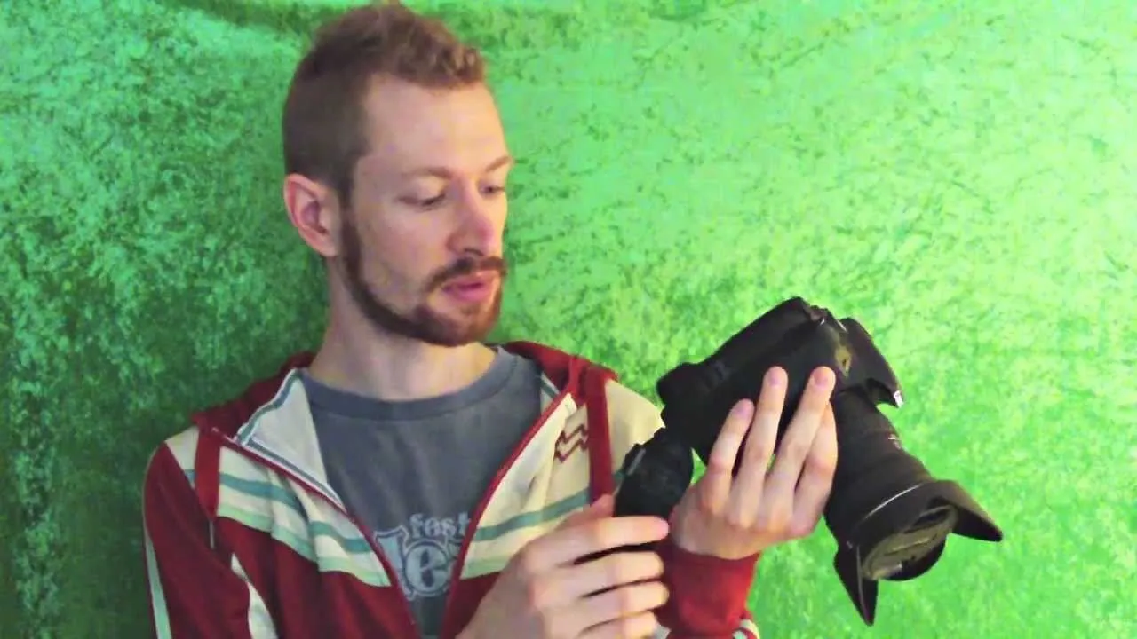 Person holding a camera against a green backdrop.