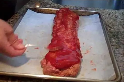 Meatloaf being glazed with ketchup on a baking tray.
