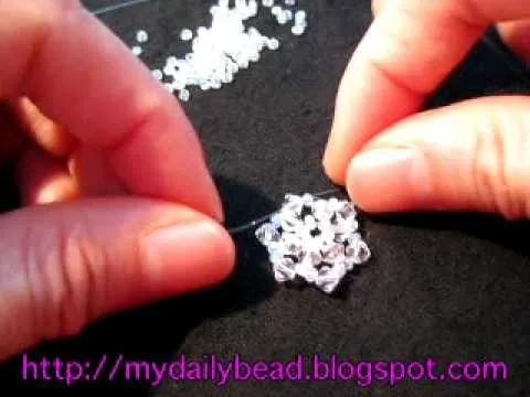 Hands creating a beaded design on a black surface.
