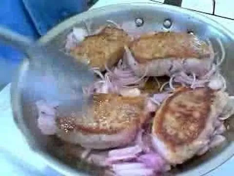 Pan-frying slices of meat with onions in a skillet.