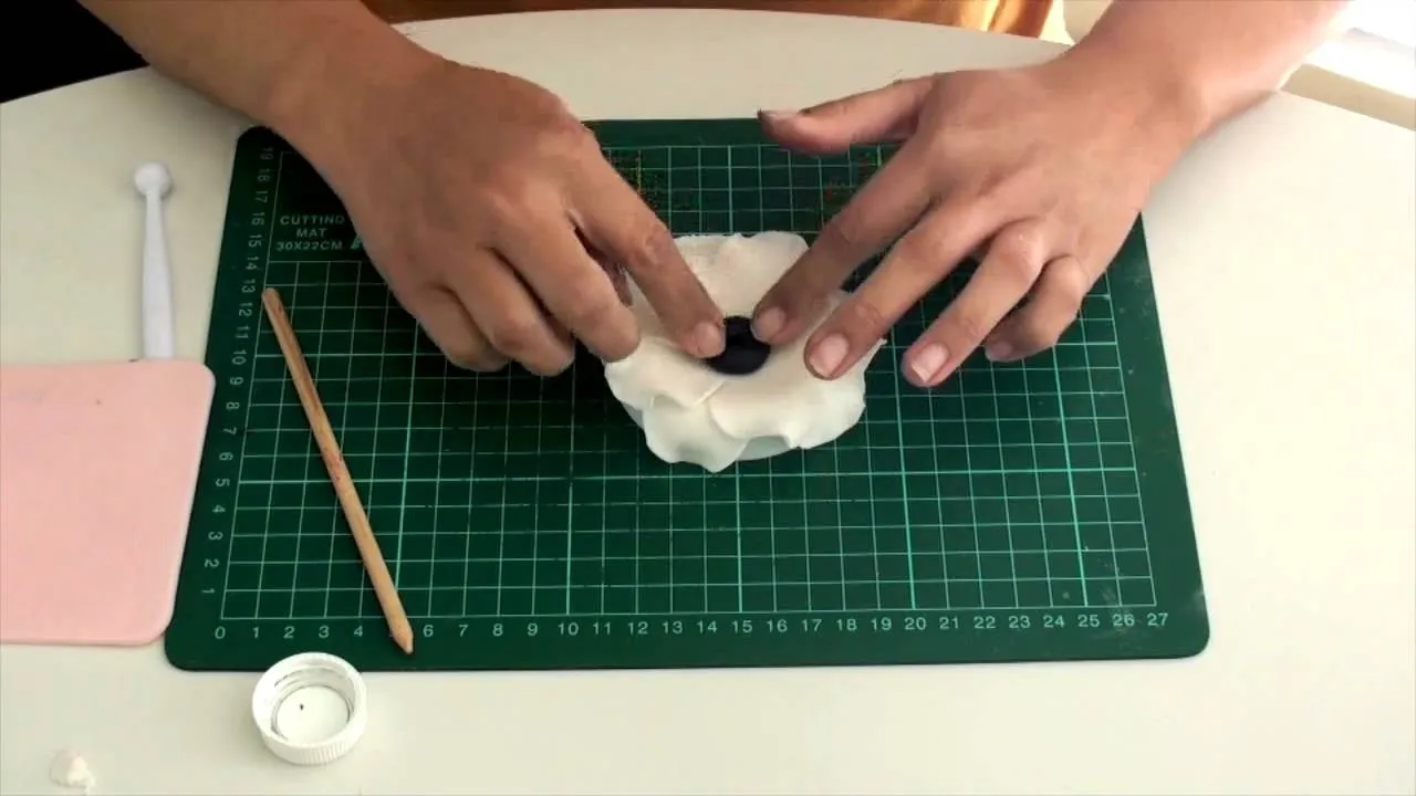 Person shaping a flower from modeling clay on a cutting mat.