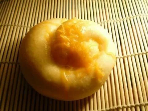 Steamed bun with a creamy filling on a bamboo mat.
