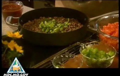Cooked ground meat with chopped green onions in a skillet, surrounded by bowls of chopped vegetables and sauce.