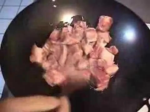 Raw meat cubes in a black frying pan.