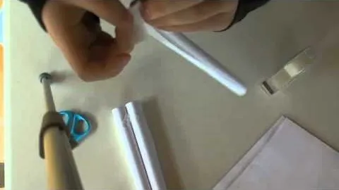 Person assembling white tubes on a table with scissors and paper.