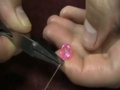 Hand holding a pink gemstone while using pliers to manipulate wire.