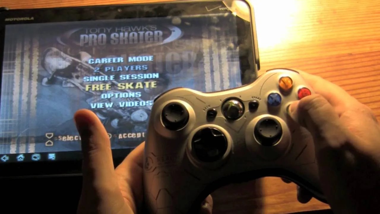 Person holding a game controller in front of a tablet displaying a video game menu.