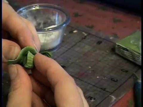 Hand holding a green craft material next to a bowl of powder on a table.
