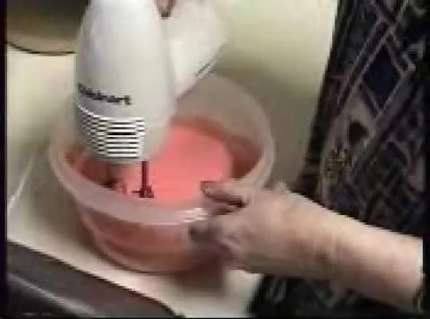 A person using a hand mixer to blend pink cake batter in a mixing bowl.