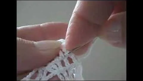 Close-up of a hand crocheting with a needle and white yarn.