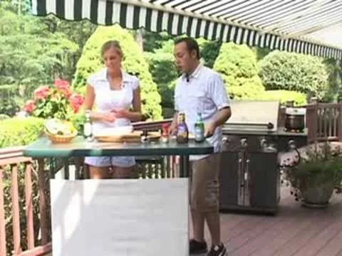 Two people preparing food at an outdoor kitchen with a grill in the background.