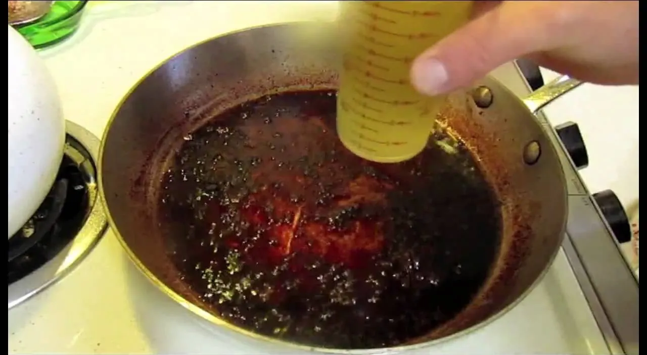 Adding seasoning to a pan of dark sauce.