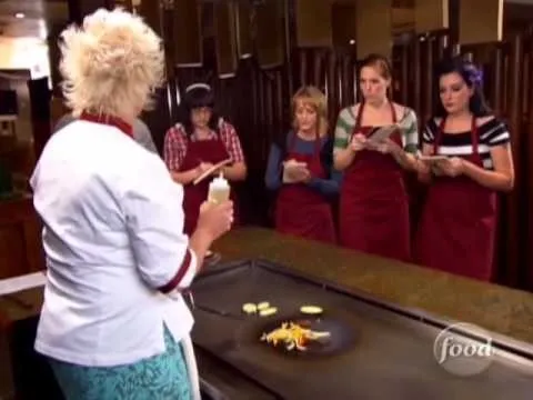 Cooking class with instructor demonstrating on a griddle, while students observing and taking notes.