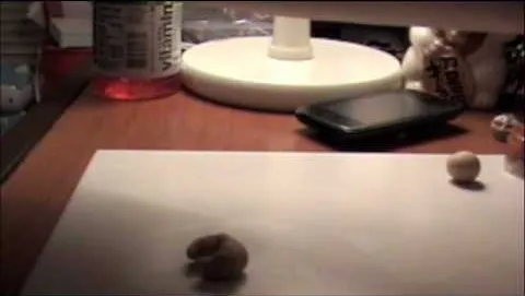 A small clay figure on a workspace with a lamp and a phone in the background.