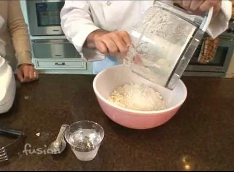 Chef pouring ingredients into a mixing bowl in a kitchen setting.