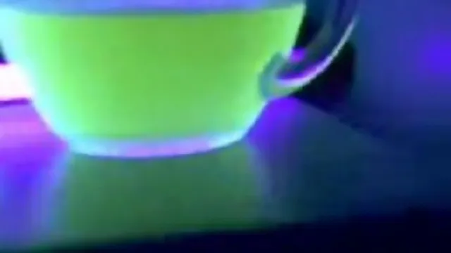 Fluorescent liquid in a transparent cup illuminated by ultraviolet light.