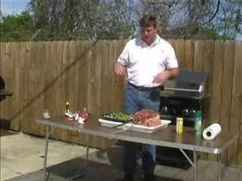Man preparing food at a backyard barbecue with a grill and various ingredients on a table.