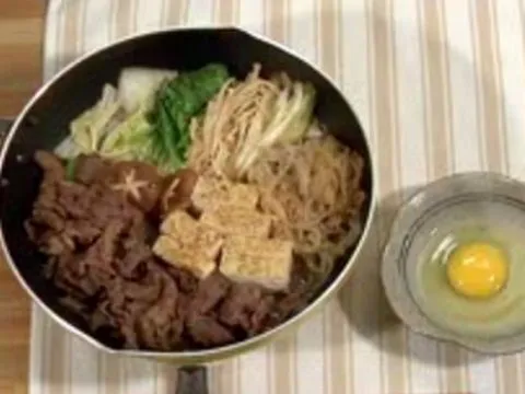 Stir-fried vegetables and beef with tofu and a raw egg in a bowl.