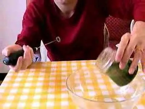 Person pouring a green substance from a jar into a glass bowl on a checkered tablecloth.