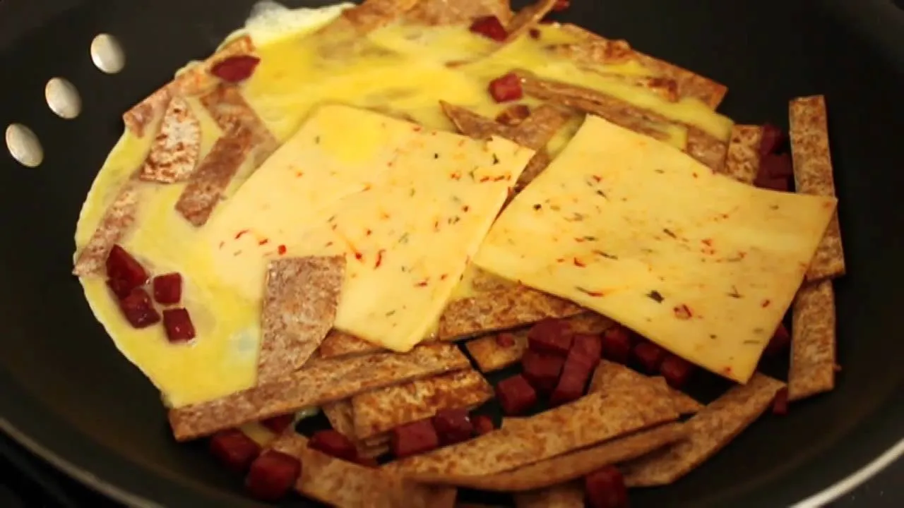 Eggs and tortillas cooking in a pan with spices and diced ham.