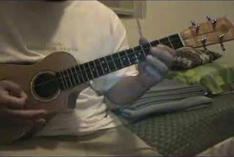 Person playing a ukulele while sitting on a bed.