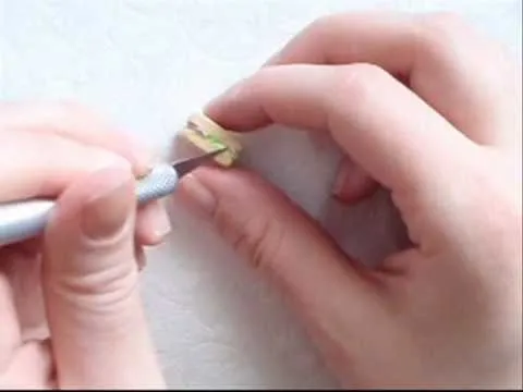 Hands carefully sculpting a small object with a craft knife.
