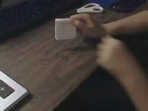 Person's hands holding a small blank paper on a wooden desk with a laptop and scissors nearby.