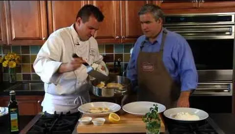 Chef plating a dish while another man observes in a kitchen setting.