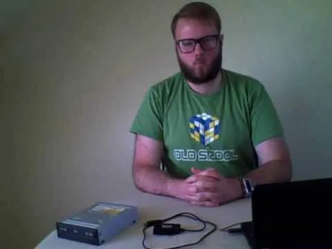 Man in a green t-shirt sitting at a table with a laptop and a device.