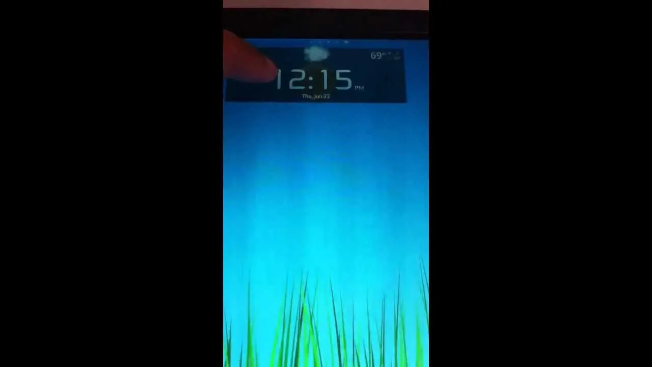 Digital clock displaying the time 12:15 against a blue background with green grass.