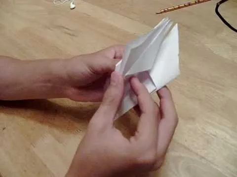 Person folding a piece of paper on a wooden surface.