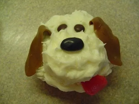 Dog face cupcake decorated with frosting and candy.