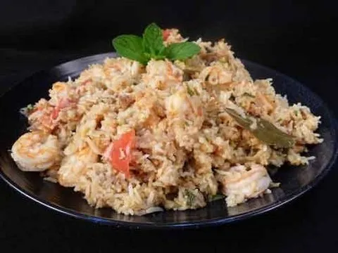 Shrimp biryani served on a black plate with fresh mint garnish.